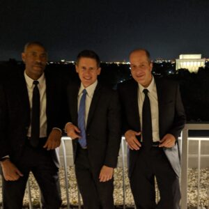Jay Frost Trio in dark suits at a roof gig with the Lincoln Memorial in the background