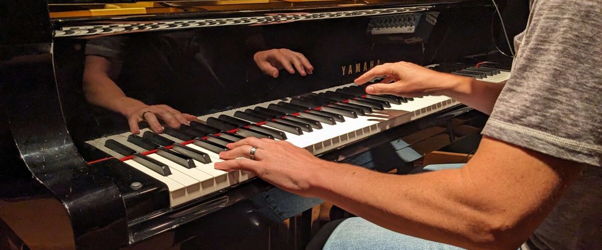 Jay Frost at Cue Recording Studio with hands reflecting in Yamaha piano